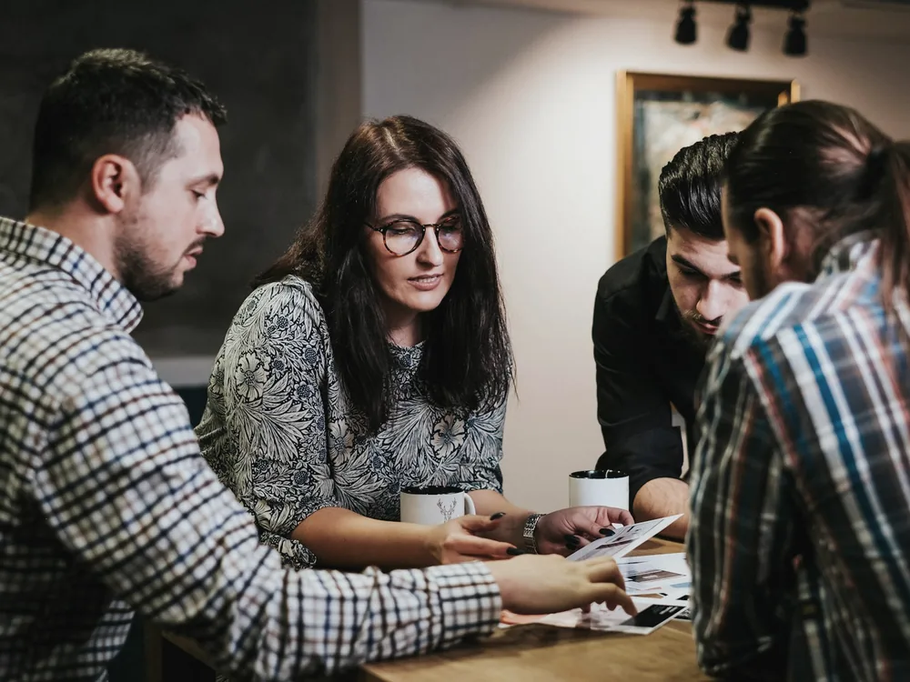 Three people reviewing printed documents and a laptop at an office table